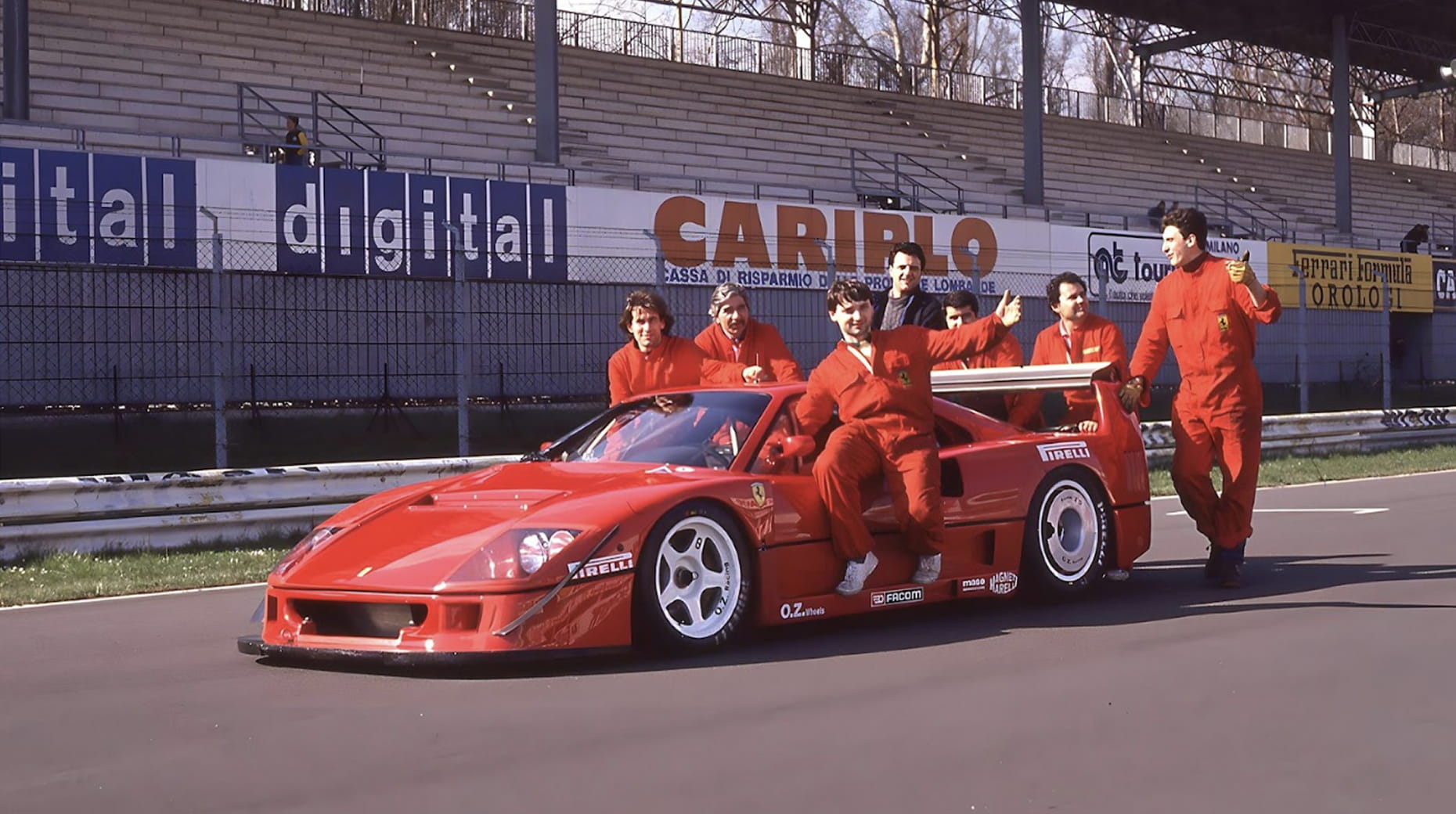 Team in red suits posing on the Ferrari F40 Competizione with Pirelli sponsorship at Monza circuit