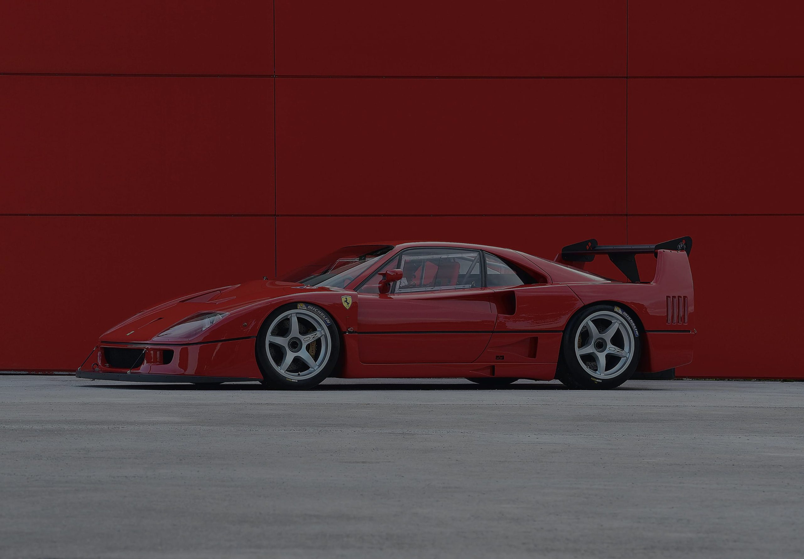 Ferrari F40 Competizione side profile with raised engine cover on red background, widescreen format